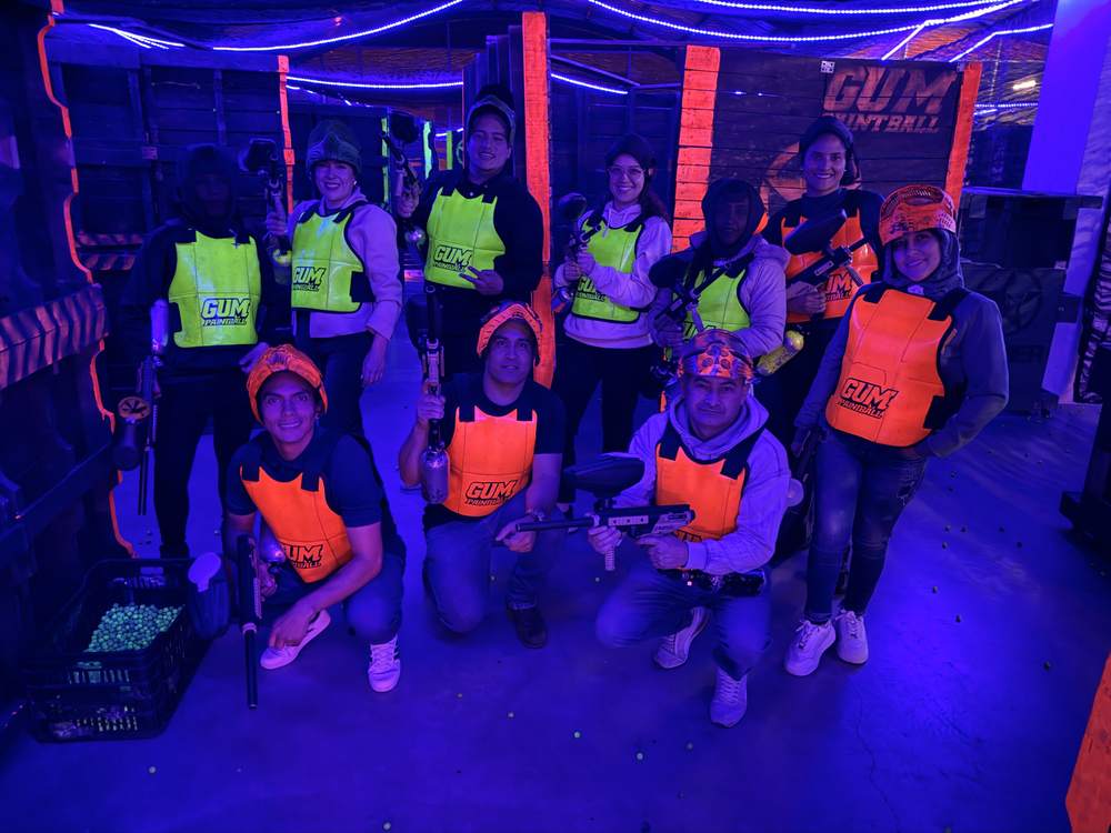 Grupo de 10 jugadores con chalecos GUM Paintball bajo luz UV y neón en Bogotá